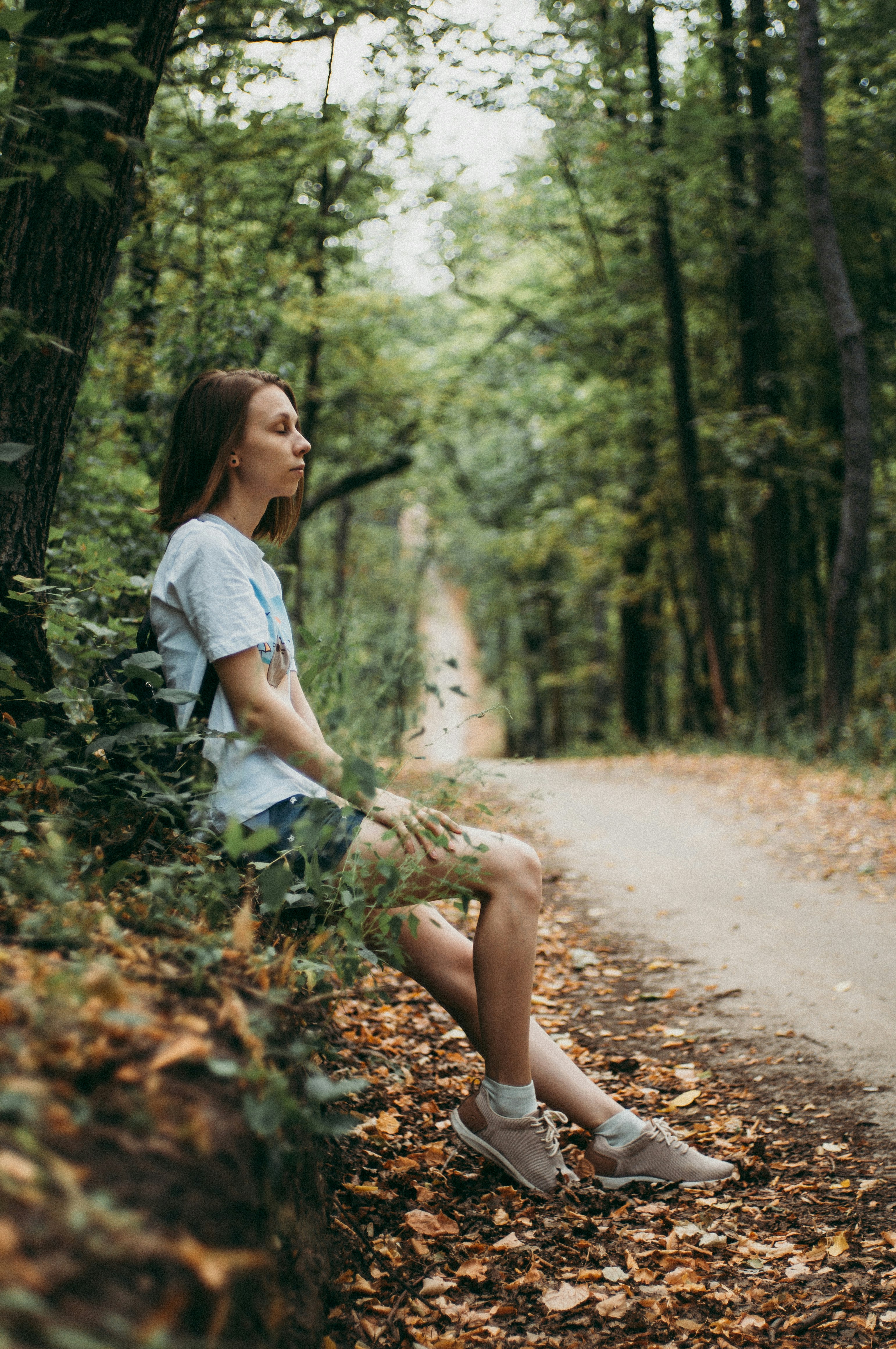 woman in white t-shirt sitting on brown dirt road between trees during daytime